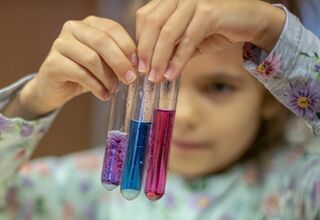 Dziewczynka przygląda się trzem próbkom z kolorowymi cieczami