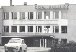 Czarno-białe zdjęcie przedstawiające budynek DK Zacisze i samochód