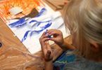 Dziewczynka z palcami w farbie i jej praca przedstawiająca łódkę