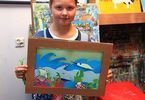 Dziewczynka trzyma pracę w tekturowej  ramce przedstawiającą świat podwodny
