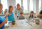 Dzieci i kobieta podczas warsztatów malowania farbami, dwoje dzieci ma kolorowe okulary na oczach