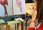 Kobieta w czerwonym swetrze maluje ptaka farbami akrylowymi