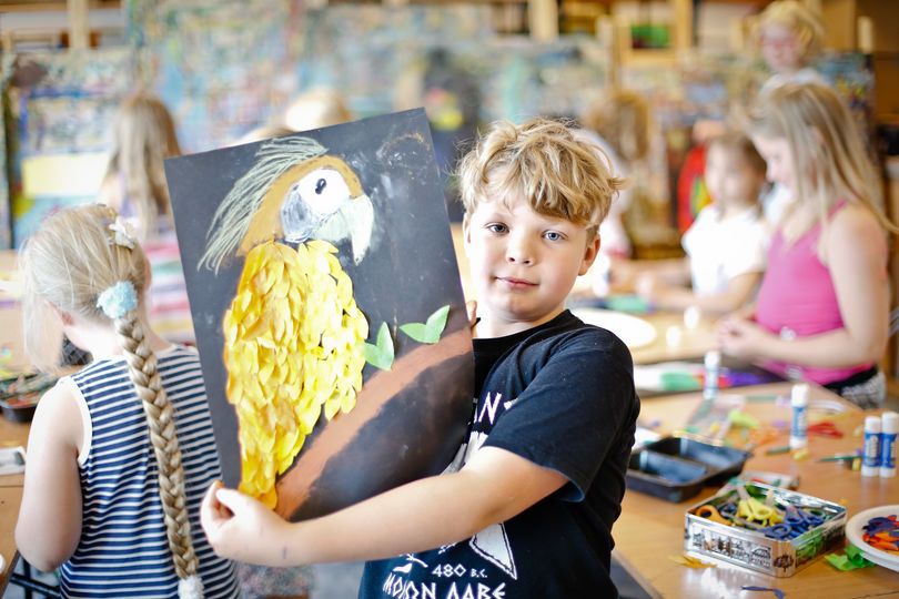 Chłopiec w czarnej koszulce trzyma pracę przedstawiającą żółtego ptaka